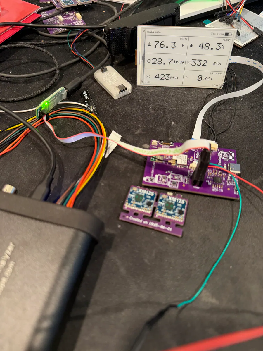 Close view of the EnviroIQ e-ink display showing temperature, humidity, pressure, CO2, and VOC index while connected to bench hardware.